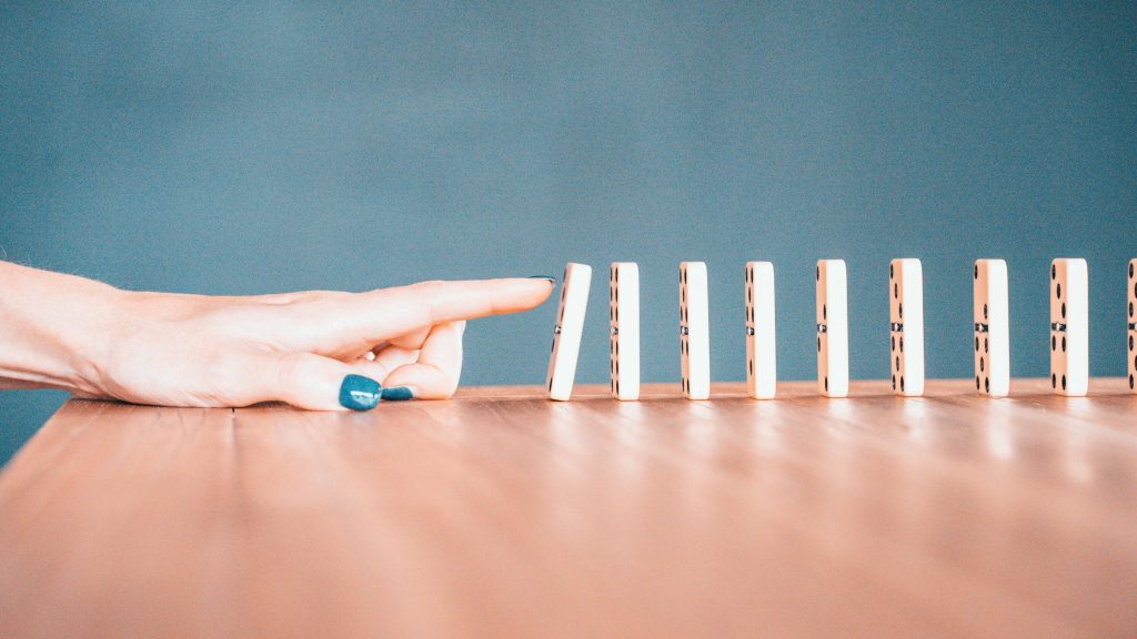 A hand pushing down a set of dominos.