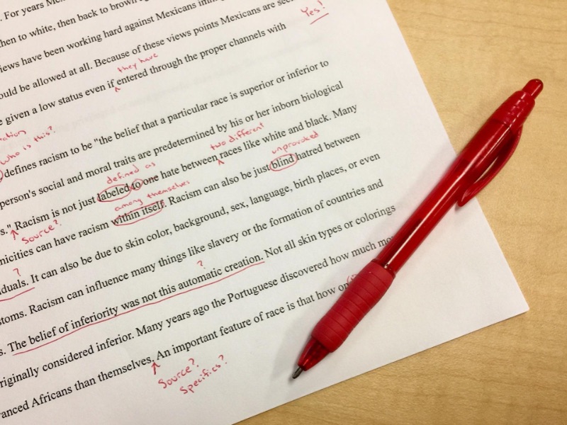 Printed document covered with notes written in red pen. A red pen is on top of it.
