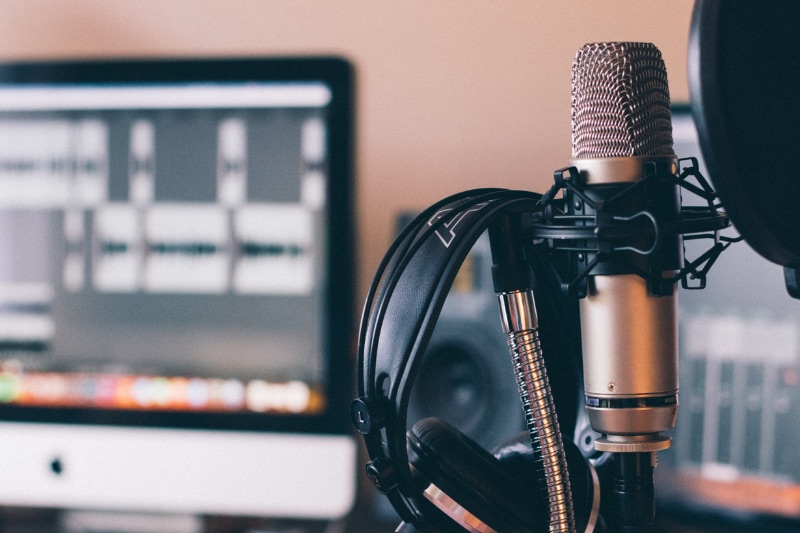 A mic and headphones in front of a Mac with a digital audio workstation on screen