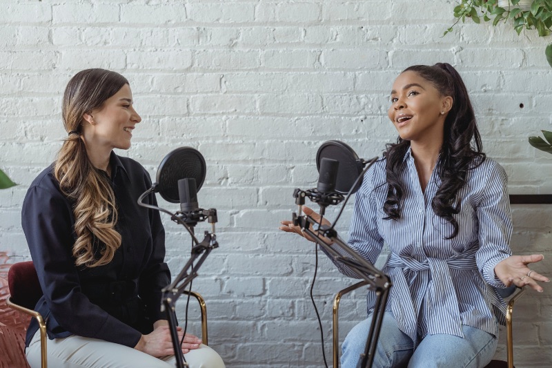 Two women in front of microphones recording a podcast together