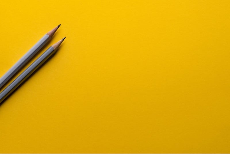 A plain yellow background interrupted by two blue pencils