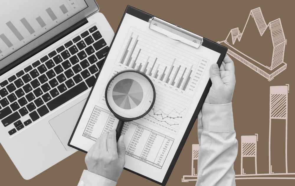Hand holding a clipboard with charts and graphs and a laptop under